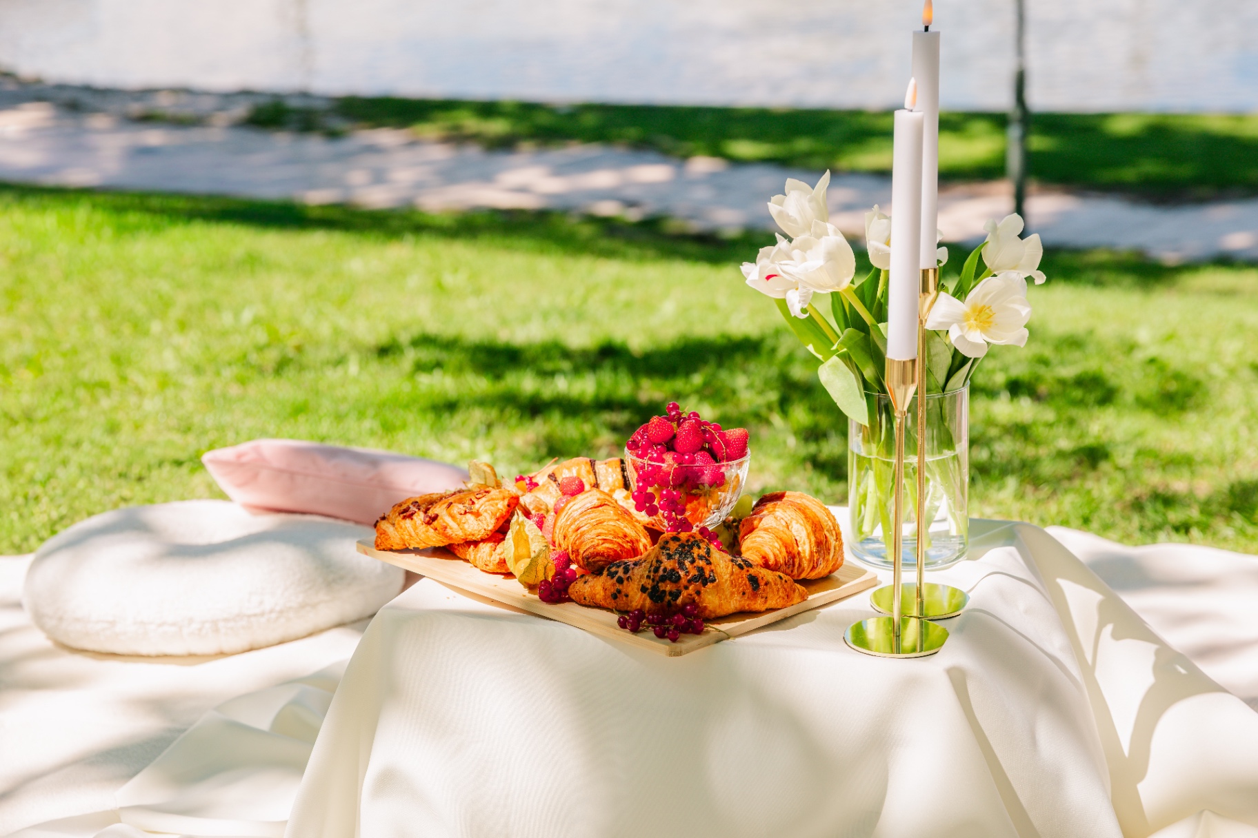 Pastry board with croissants and berries beside white tulips on a sunlit picnic table