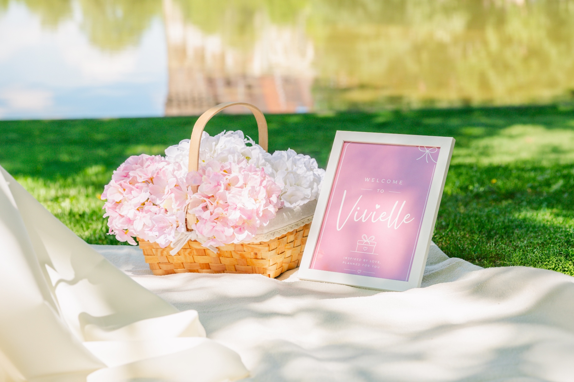 Pink hydrangea basket beside a Vivielle welcome sign on a lakeside picnic blanket
