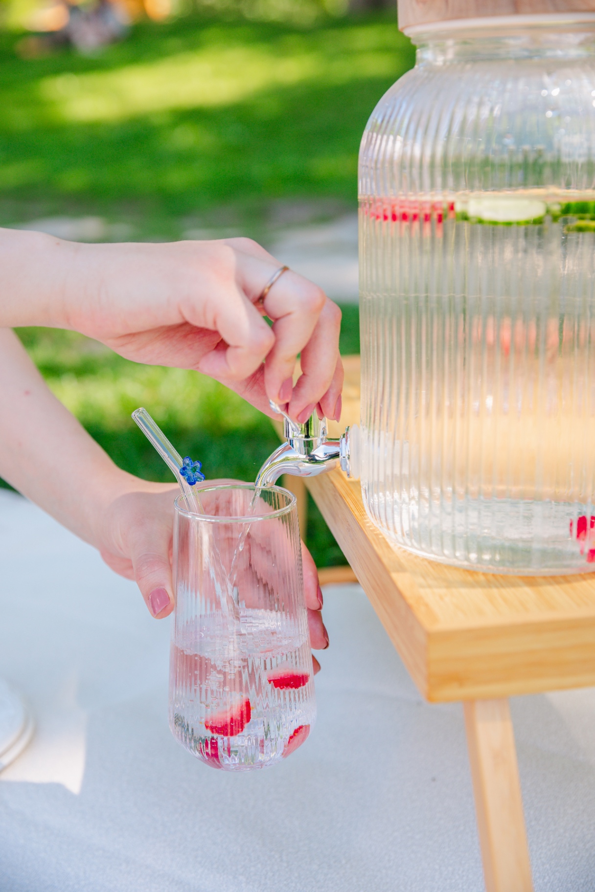 Glass dispenser pouring infused water into a fluted glass with a blue flower straw
