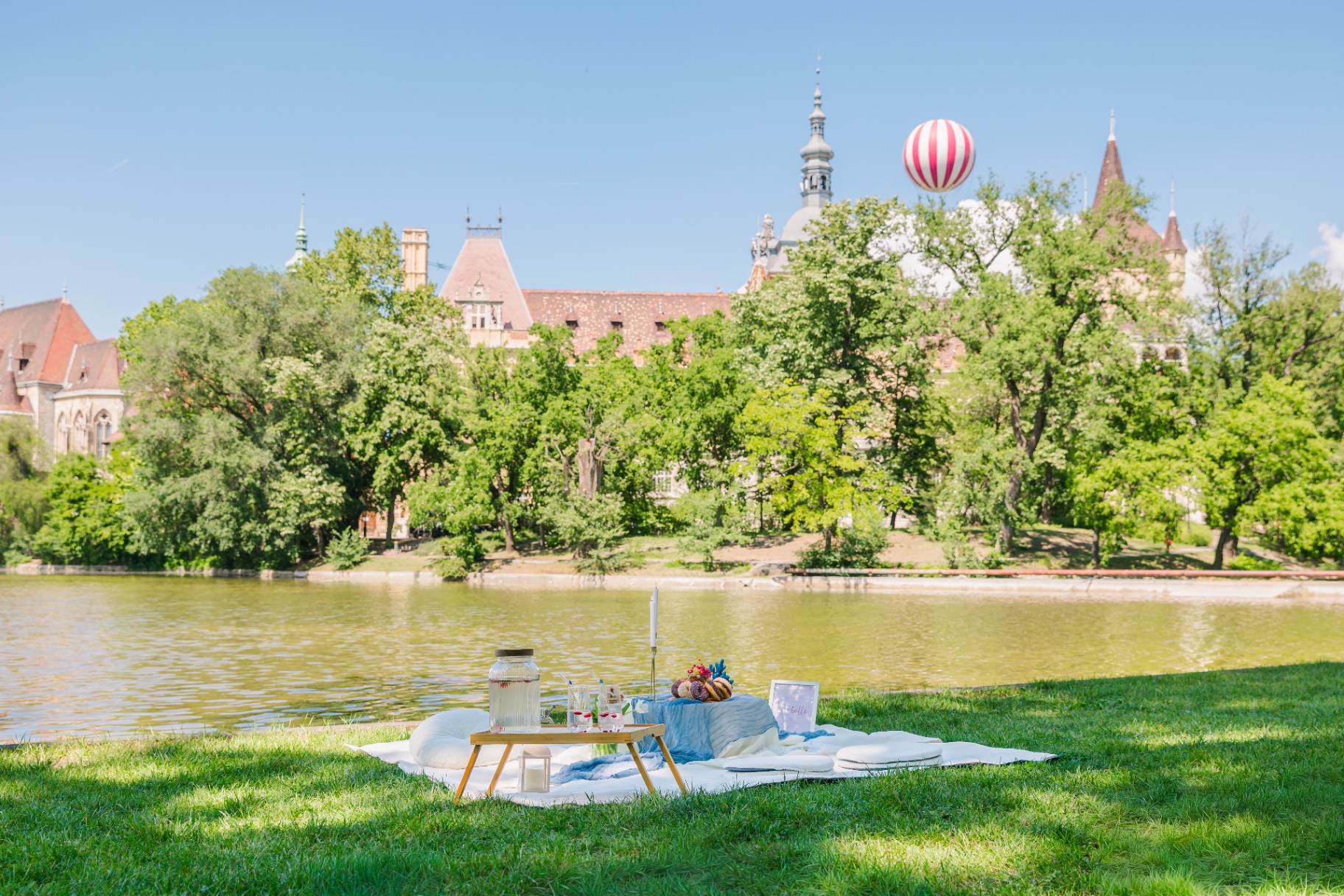 Lakeside picnic with blue gauze runner and striped balloon overlooking Vajdahunyad Castle