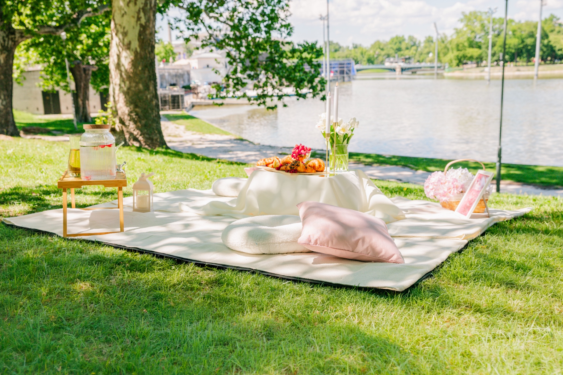 Riverside picnic blanket with pink cushion, lantern and floral basket