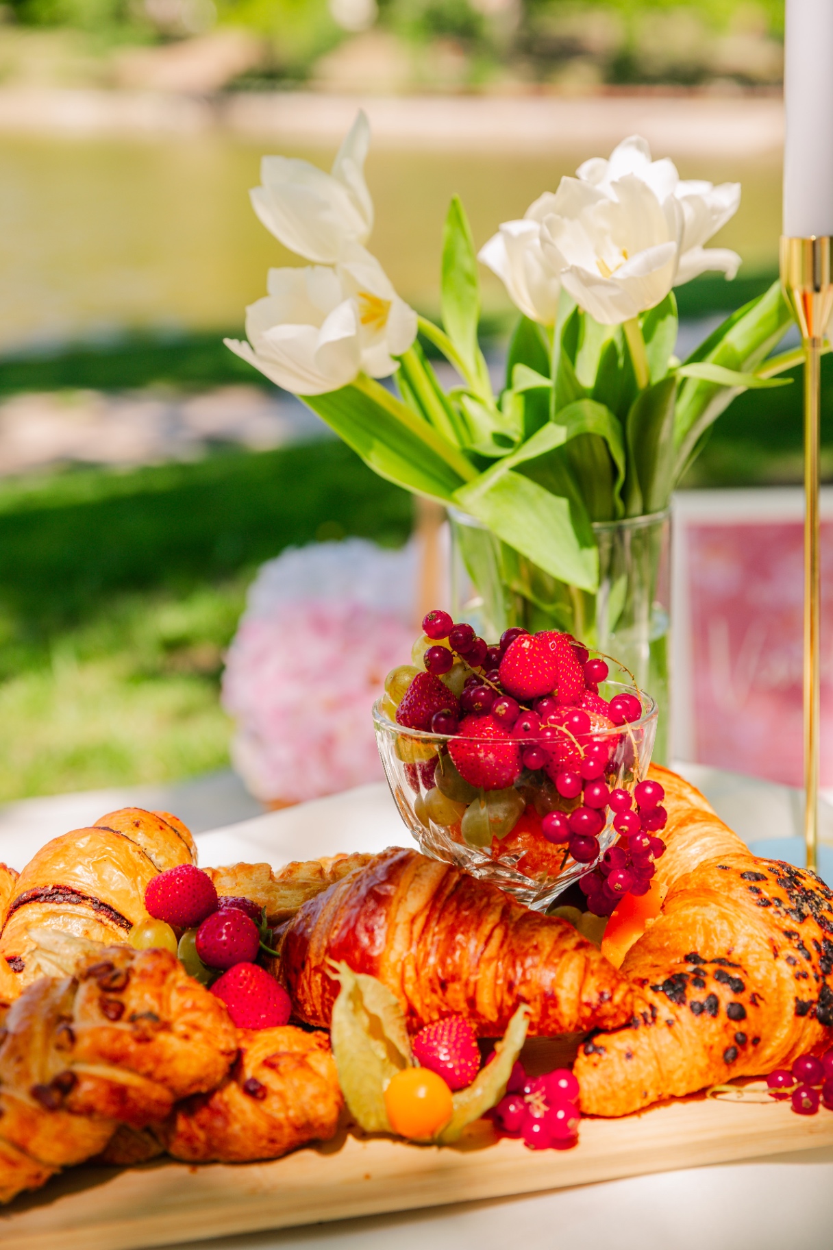 White tulips beside a fruit cup and croissant platter in the sunlight